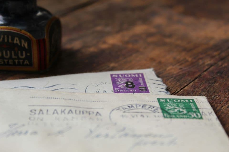 Two old Finnish envelopes on a wooden table, each carrying a different postage stamp and a Tampere postmark, with an ink bottle behind them