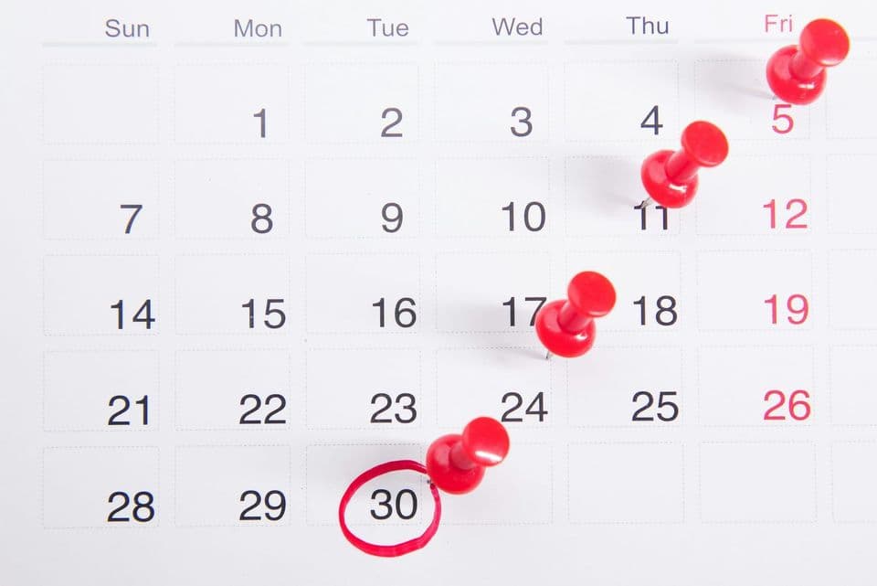 A wall calendar with red pushpins stuck into several dates and the thirtieth circled in red marker