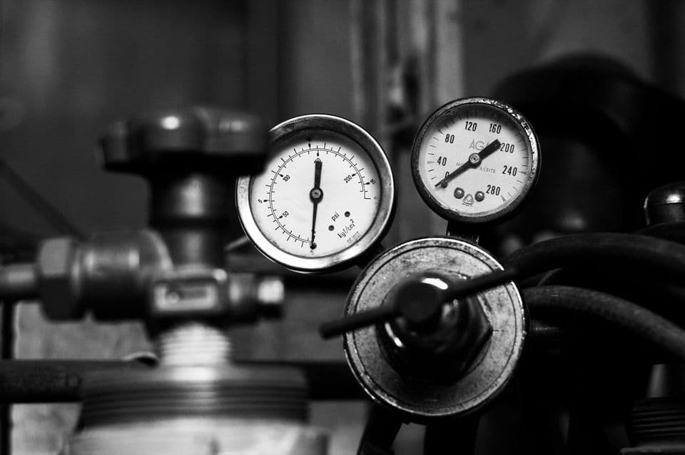Two analogue pressure gauges on a gas regulator photographed in black and white, one dial marked in psi, with a valve handwheel below them