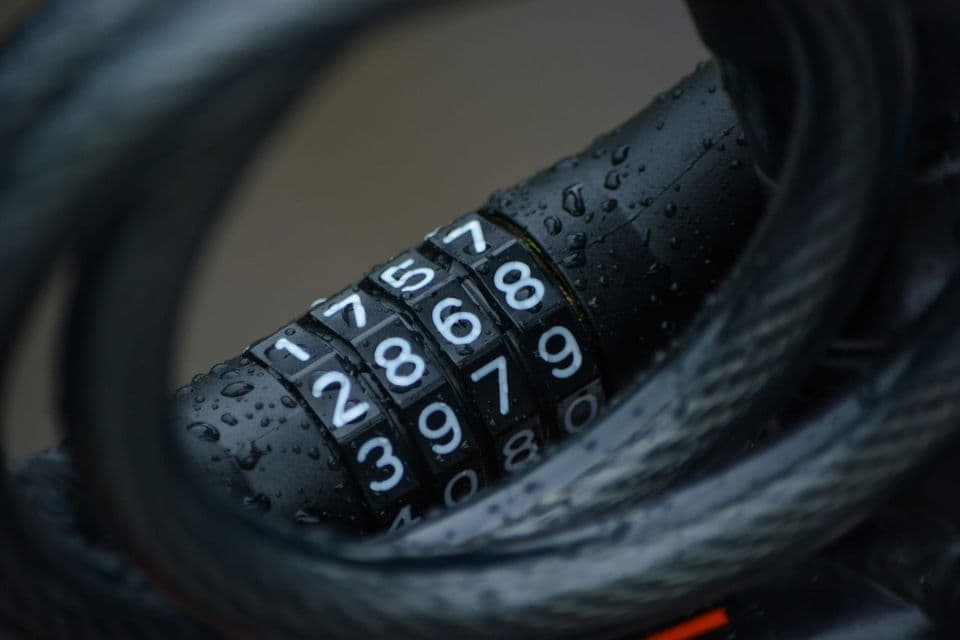 Close-up of a rain-beaded four-dial combination lock coiled in its steel cable, every dial set to a different digit