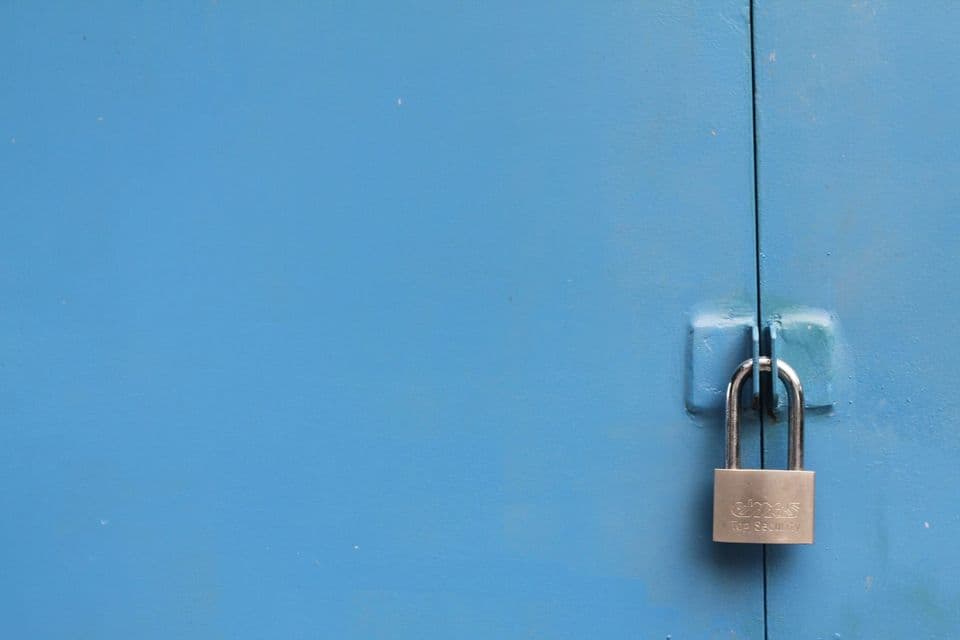 A single brass padlock closed on the hasp of a plain blue metal door