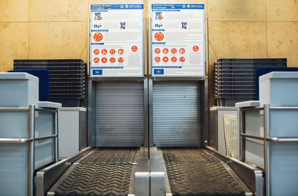Two empty baggage belts at an airport check-in desk, with panels of baggage and dangerous-goods rules posted above them in German and English