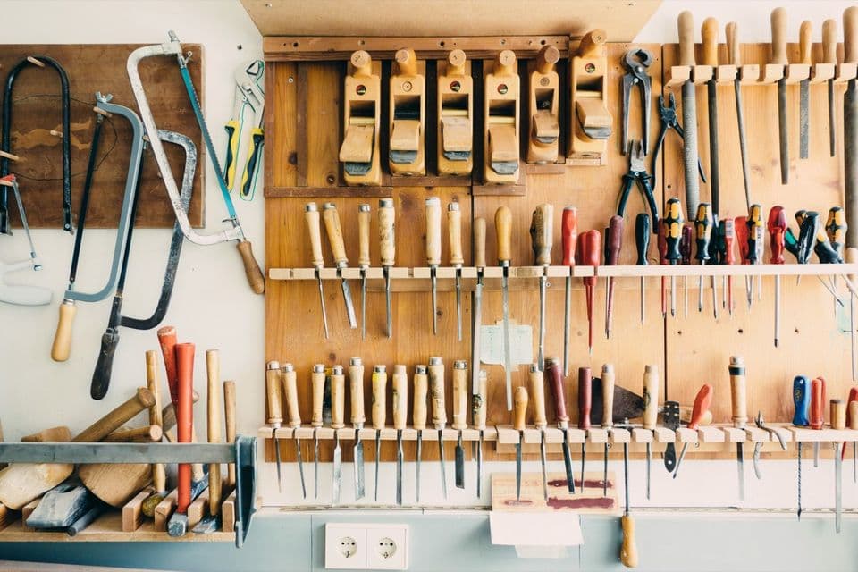 A workshop wall rack holding rows of chisels, hand planes, saws and screwdrivers, each tool in its own slot