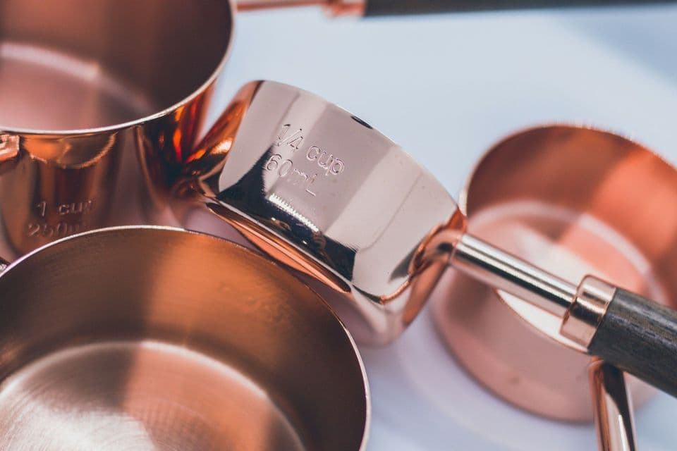 Close-up of copper measuring cups of different sizes, one stamped 1/4 cup 60 mL and another 1 cup 250 mL