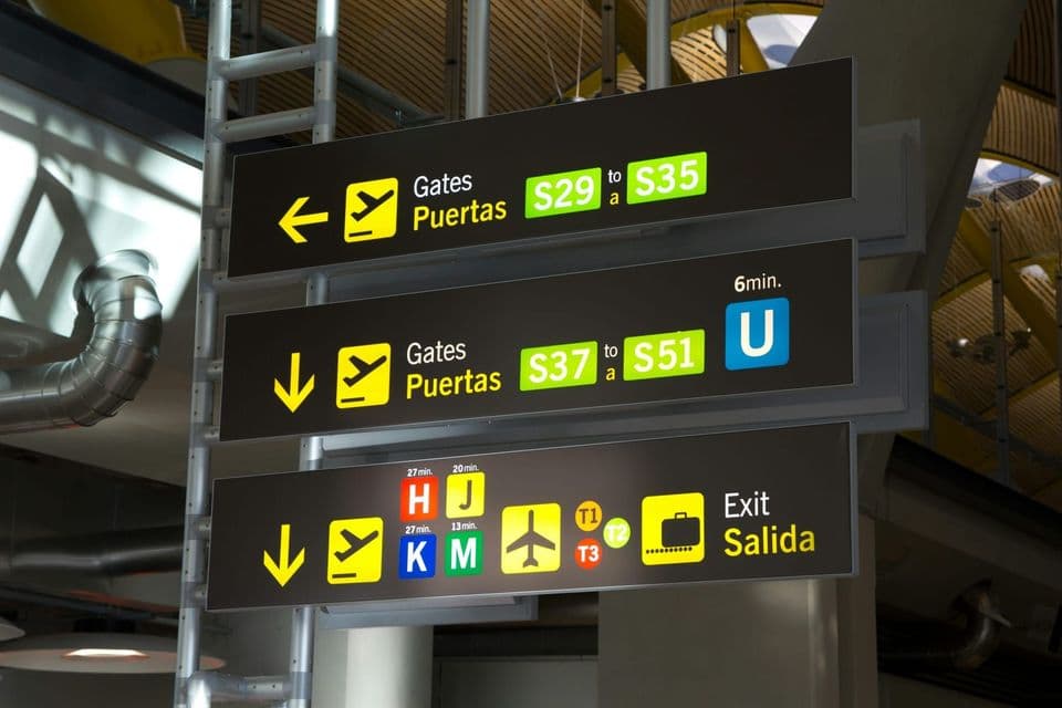 Overhead airport signage pointing to two separate ranges of departure gates, one arrow left and one arrow down