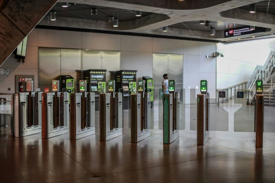 A row of fare gates standing across an empty station concourse, each one showing its own green arrow