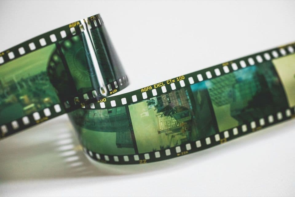 A curled strip of 35mm colour negative film on a white surface, green-cast frames and AGFA edge markings in focus