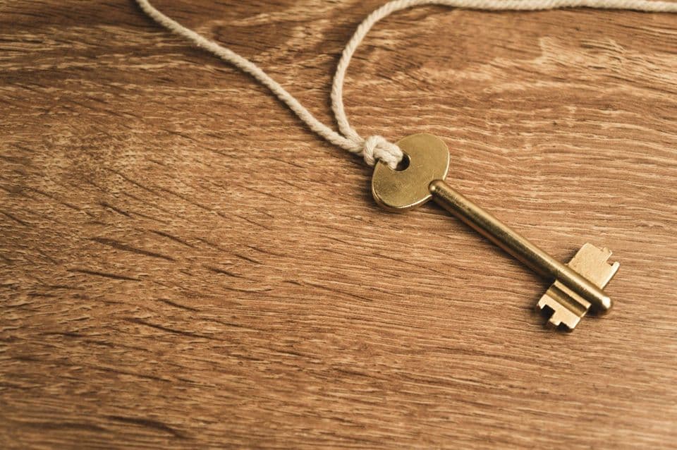 A single brass key on a white string lying on a wooden table, photographed at an angle with shallow depth of field