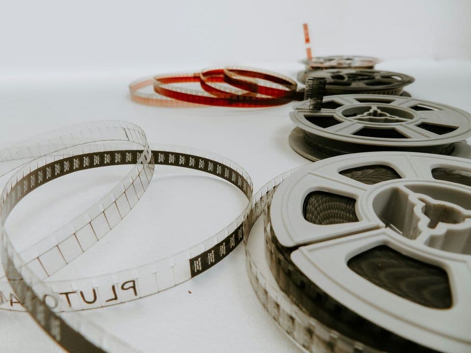 Reels of 8 mm film lying on a white surface with loose strips of film curled beside them, one clear strip carrying the word PLUTO in reversed lettering