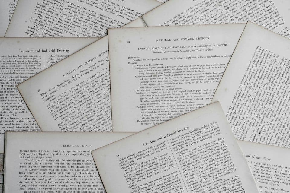 Pages torn from old printing and drawing manuals fanned out across a table, every one of them dense with printed text and section headings